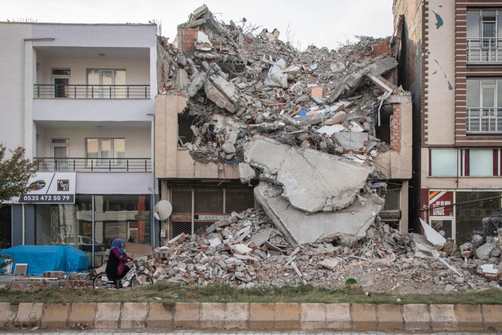 Woman on a bicycle passes a building which collapsed during the February 2023 earthquake. 